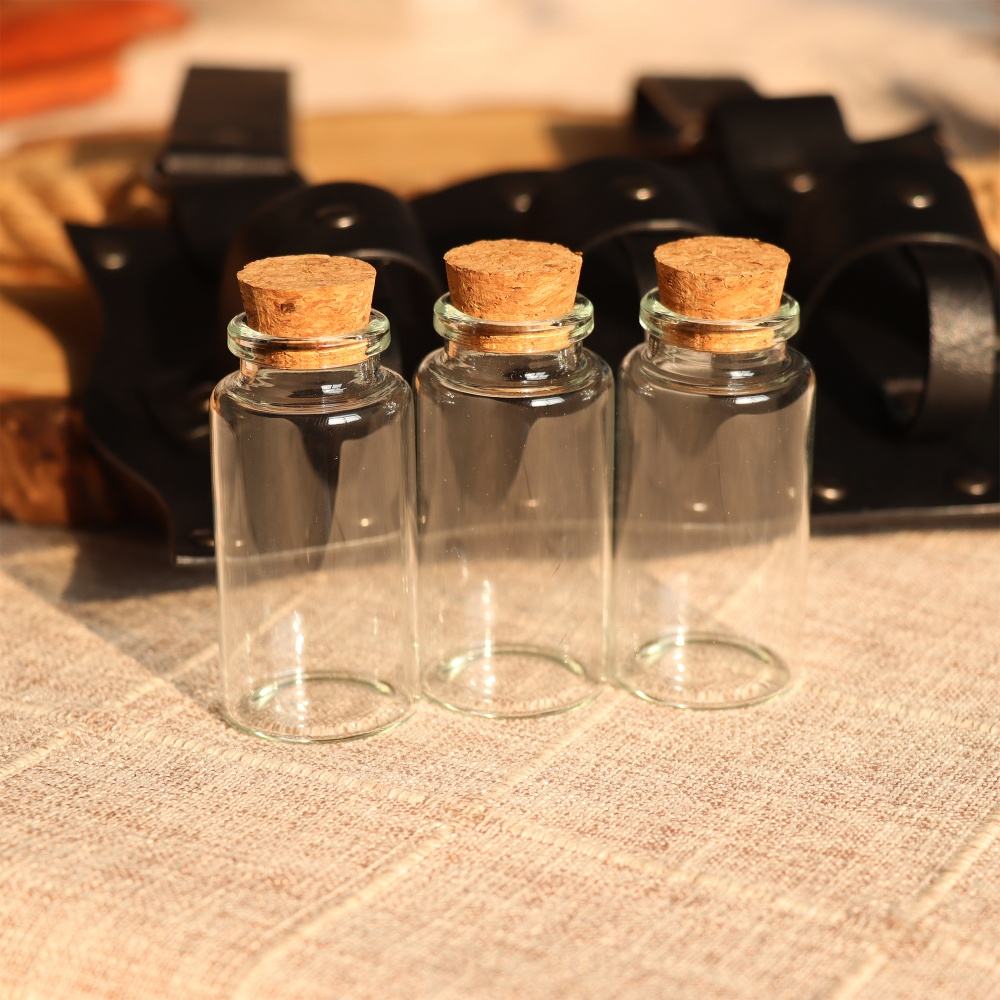 Three glass bottles with cork stoppers on a cloth. Behind the bottles is a black, leather belt pack.