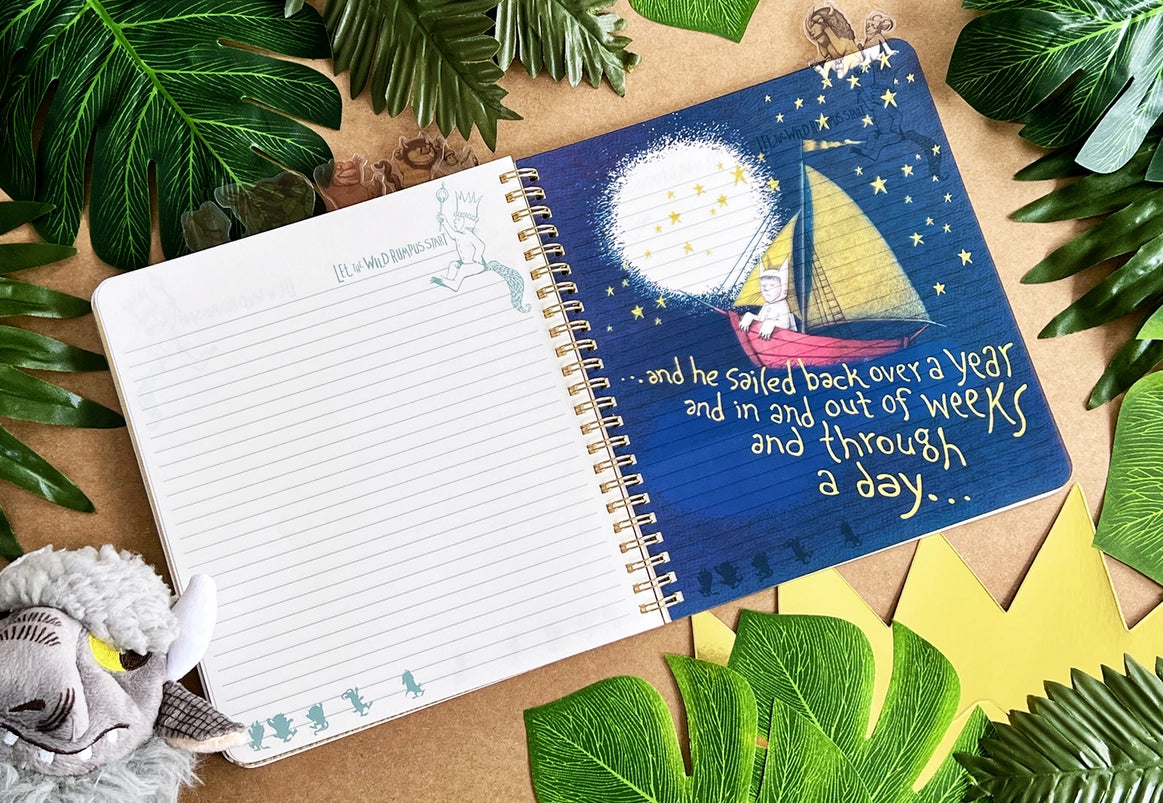 A page from the book showing Max in a red sailboat against a dark blue sky. Yellow text says "and he sailed back over a year and in and out of weeks and through a day." The journal is on a table surrounded by leaves and a goat puppet.