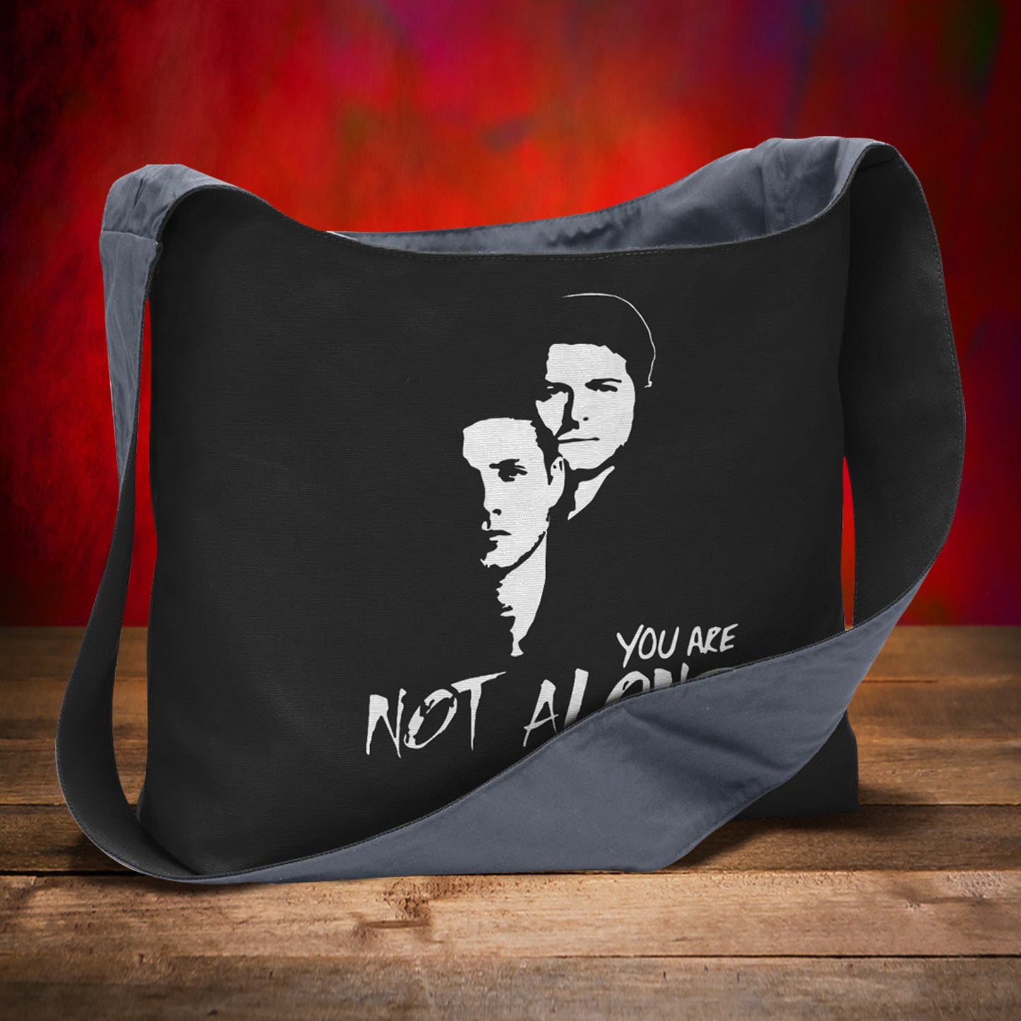 Black messenger bag with a graphic design and text on a wooden surface with a red background