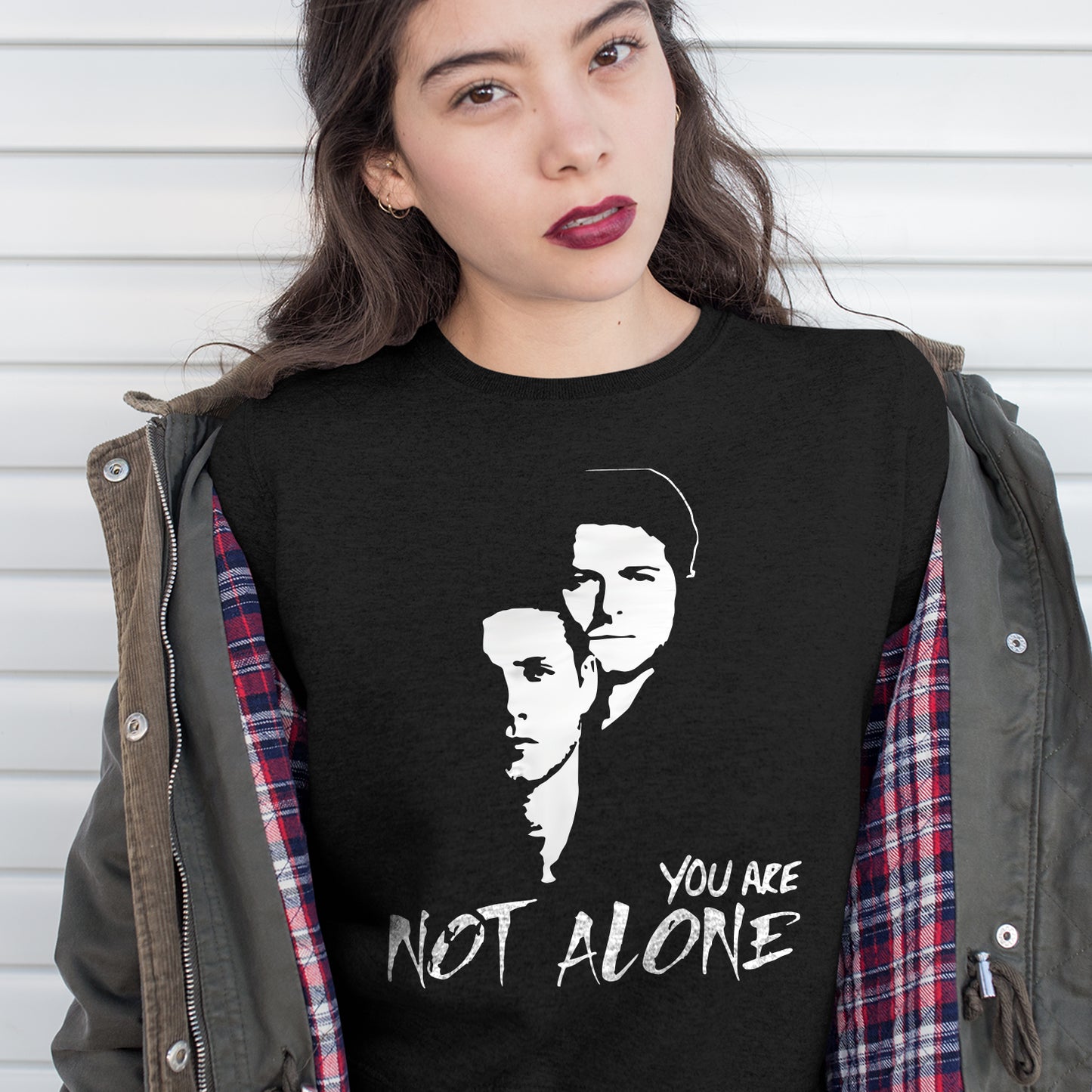 Person wearing a black t-shirt with a graphic design and text 'You Are Not Alone' against a white background.