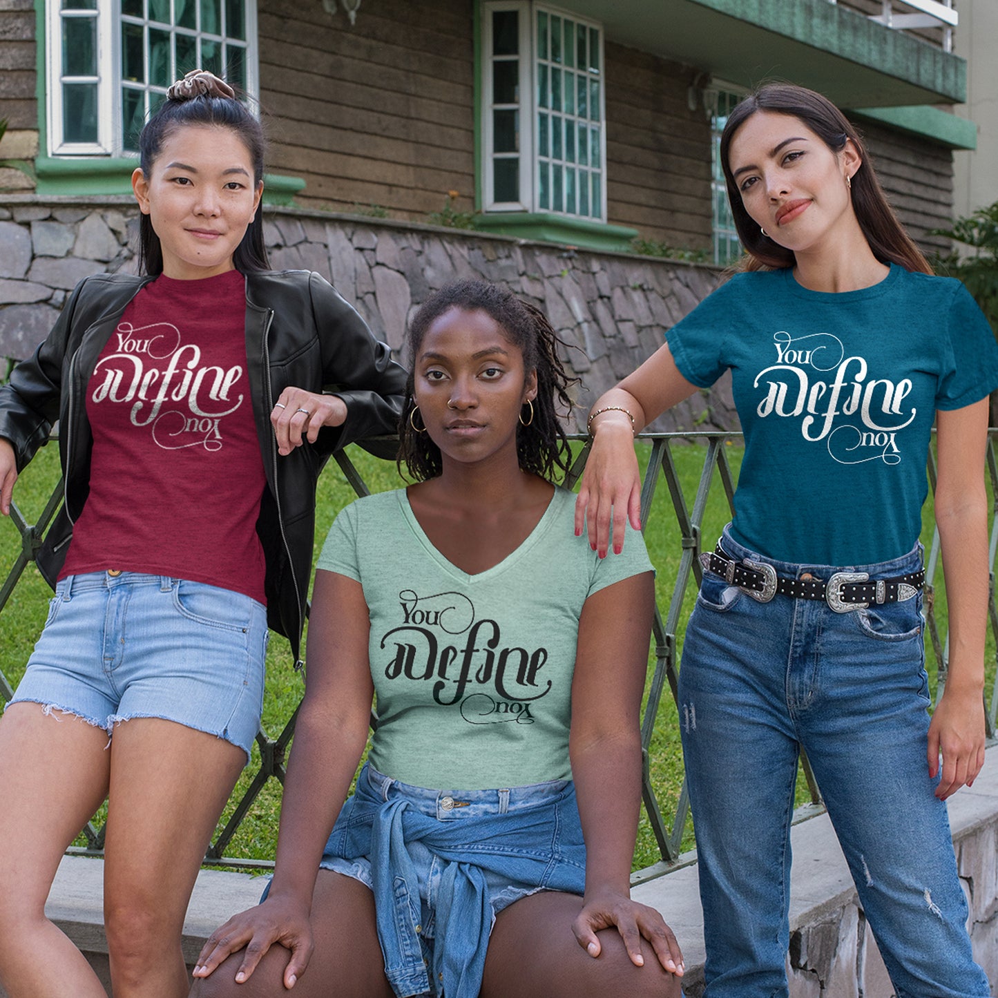 Three female models leaning on a metal gate in front of a house. Each is wearing a T-shirt with scripted text that says "You define you." The font is designed to look the same rightside up and upside down. Each model's shirt is a different color: dark red, teal, and sage green.