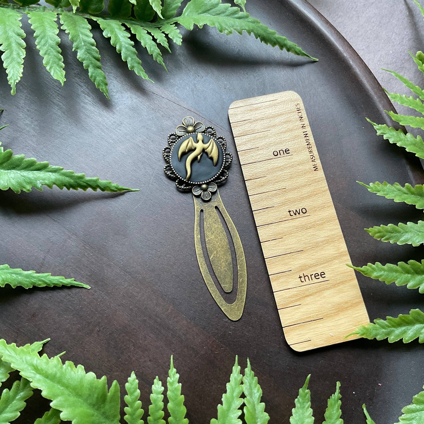 Dragon-themed bookmark and wooden ruler on a dark surface with green leaves around