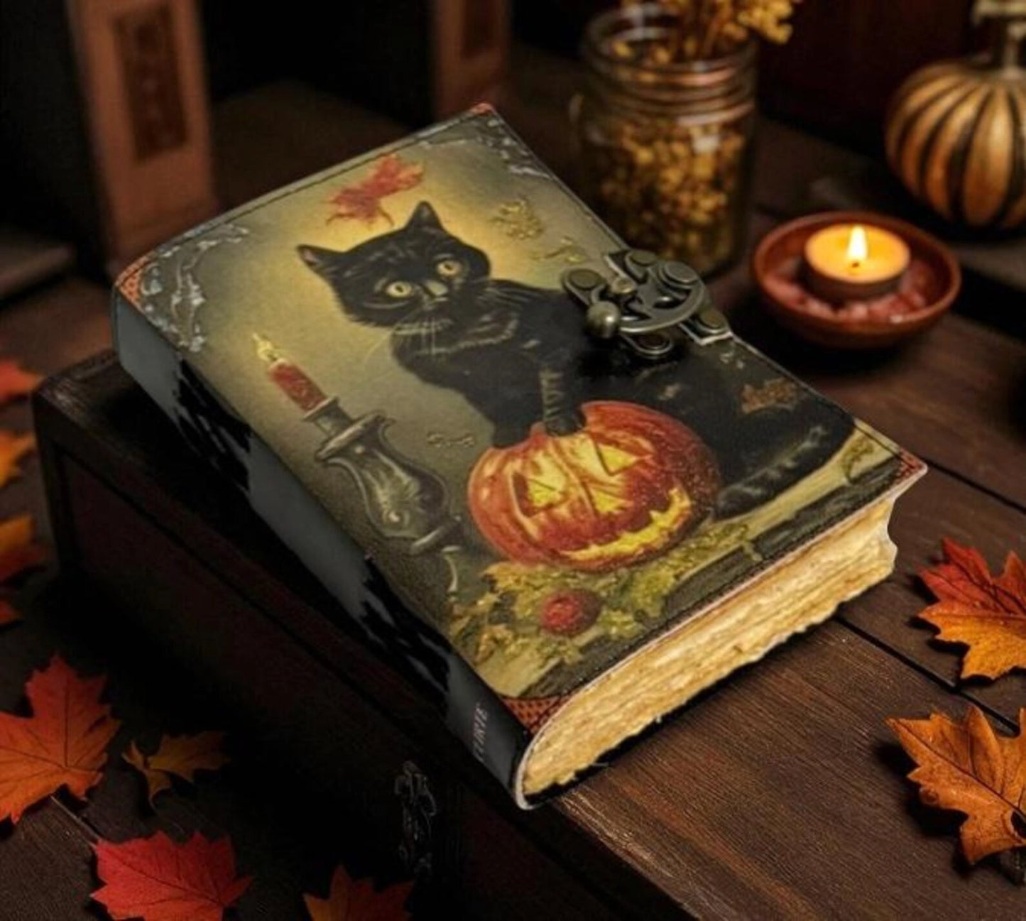 A leather journal on a wood table, next to lit candles. The cover depicts a black cat standing on a Jack-o-lantern.