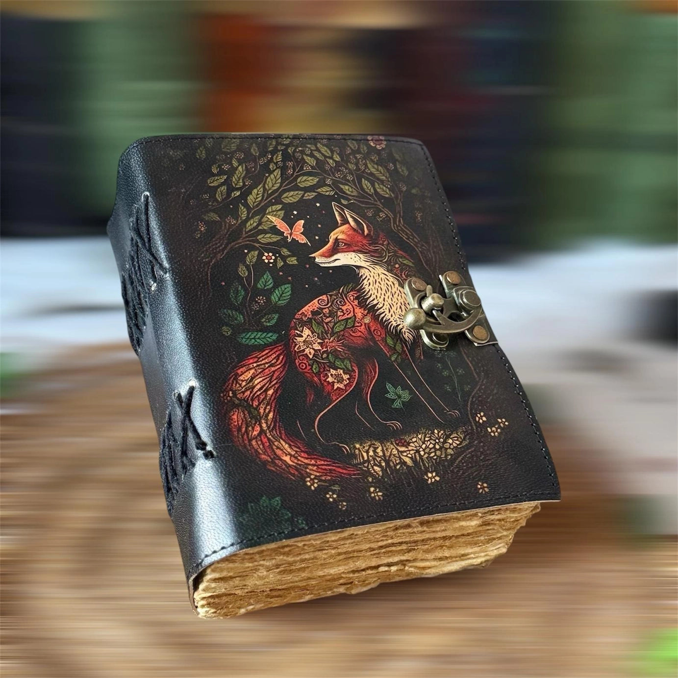 A leather journal on a wooden table. The cover depicts a red and white fox next to a dark forest.
