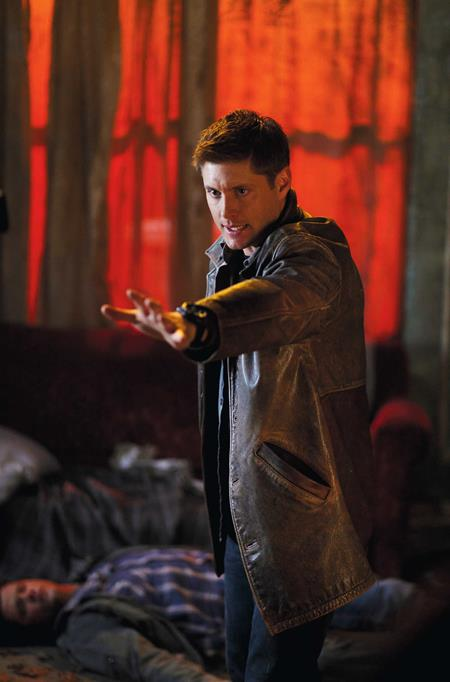 Person in a brown jacket pointing a weapon in a dimly lit room with red lighting.