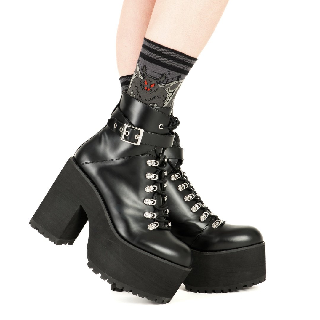 Black platform boots with high heels worn by a person on a white background