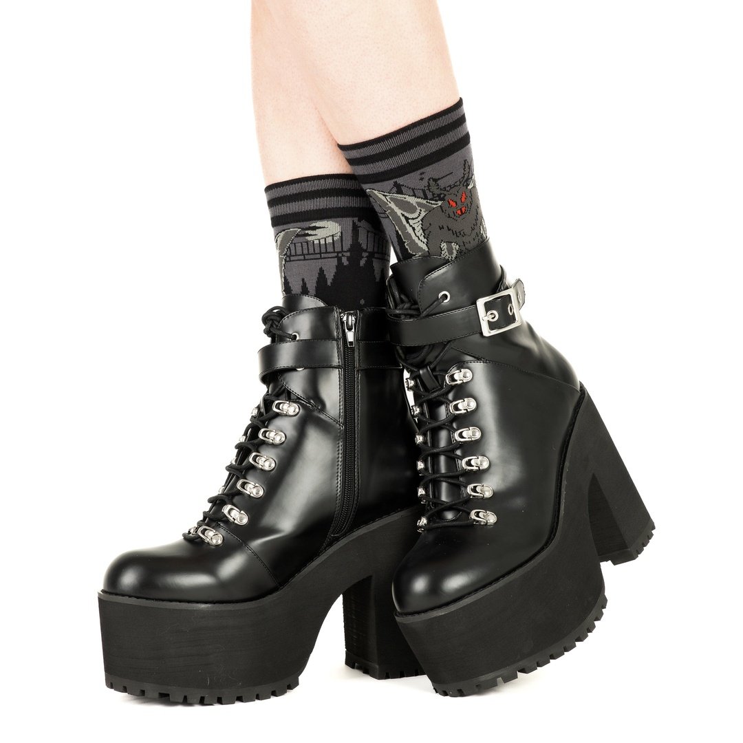 Black platform boots with high heels worn with patterned socks on a white background