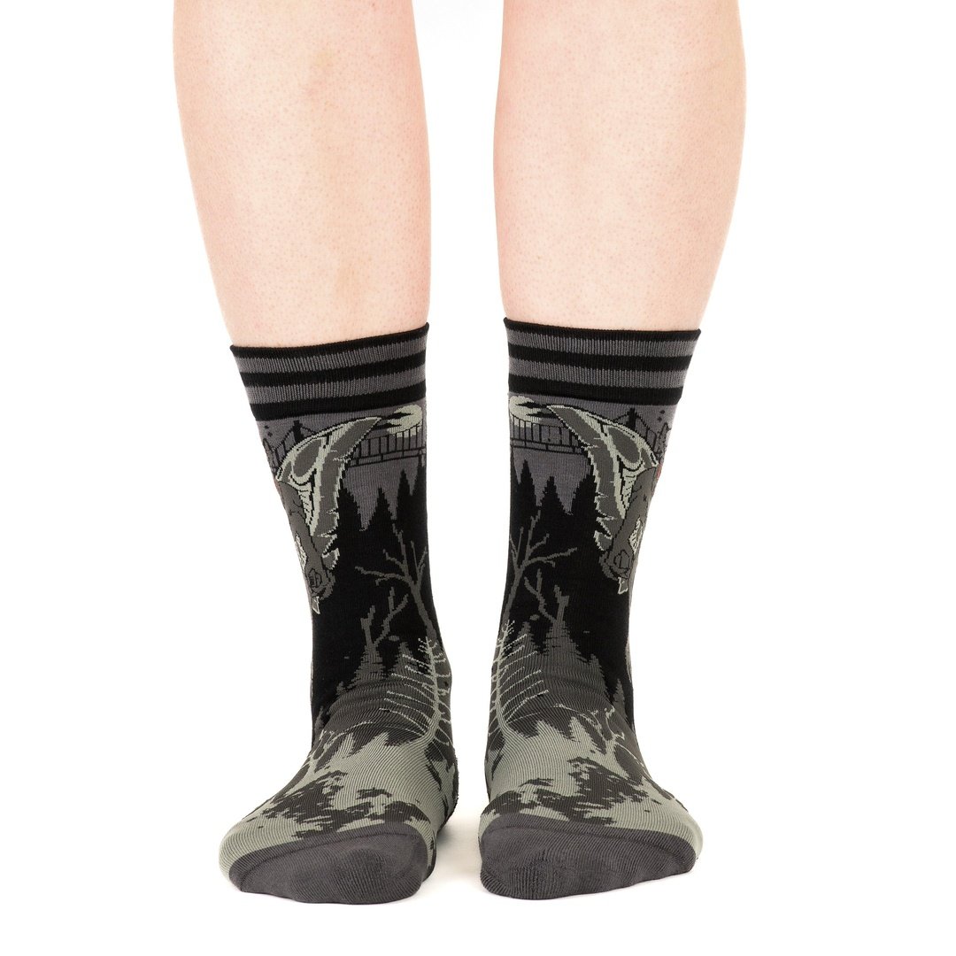 Gray forest-themed socks with black stripes worn by a person on a white background