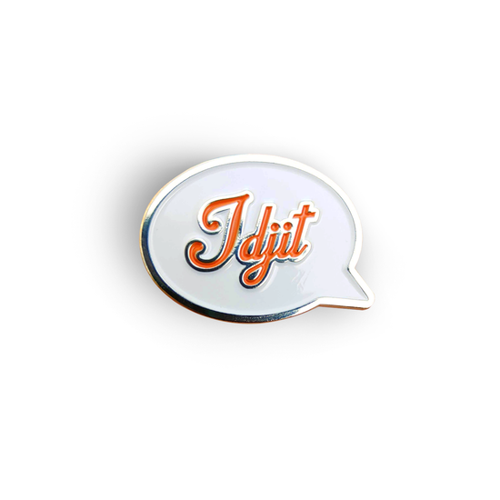 A silver pin with a white front in the shape of a speech bubble. The word "Idjit" is written in orange script font.